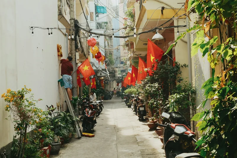 A narrow alley in Ho Chi Minh City with parked motorbikes, plants and Vietnamese flags